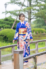 A local city in Japan on a rainy summer day. Japanese woman wearing a blue teenage kimono walking along a traditional garden bridge.