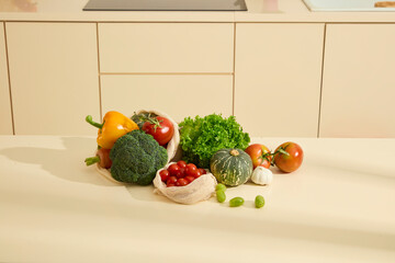 Lettuce, broccoli, bell peppers, carrots, pumpkin, tomatoes, garlic, and a mesh bag of cherry tomatoes cluster on a table. Green grapes line the other vegetables. Fresh organic food in the kitchen.