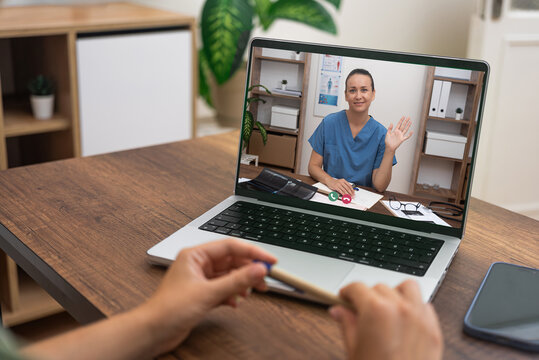 Close-up of a telehealth consultation with a nurse waving from the laptop screen.