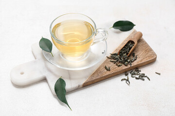 Glass cup of hot green tea and dried leaves on white background