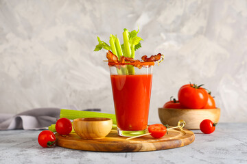 Glass of bloody mary cocktail with bacon, celery and bowl of spices on grey background