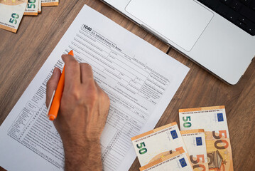 Naklejka premium Business owner fills 1040 tax form with pen documenting income and deductions to determine potential refund sitting at table with euro banknotes and laptop