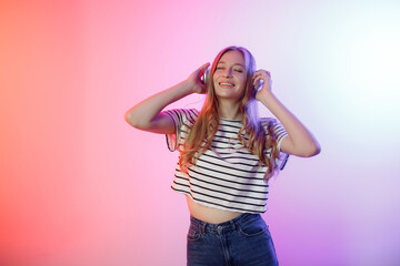 Young woman enjoying music while wearing headphones in a colorful lighting setup