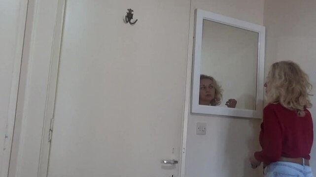 A girl in front of a mirror admires and plays with her hair. The girl is in a great mood. She is getting ready for a date