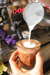 pouring milk from a milk jug to a glass of espresso coffee to create latte art