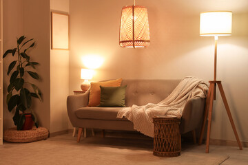 Interior of stylish living room with cozy grey sofa, coffee table and glowing lamps at evening