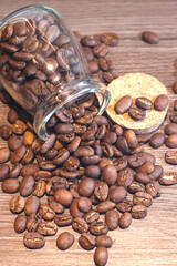 A glass jar of whole roasted coffee beans has tipped over, spilling its contents onto a rustic wooden table next to its cork lid