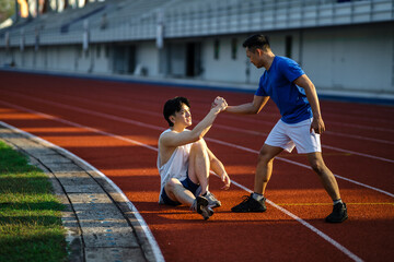 Asian man is grabbing or pulling his friend hand to help him standing up after falling on racetrack.