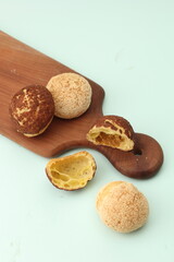 choux au craquelin pastries, some whole and some halved, are arranged on a wooden board against a light background