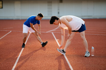 Two asian athlete men are stretching their legs and foots together on the racetrack in sports...