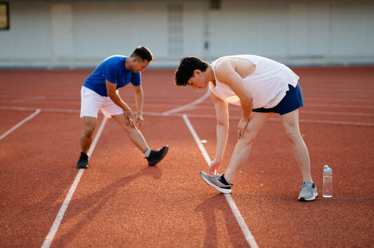 Two asian athlete men are stretching their legs and foots together on the racetrack in sports stadium.
