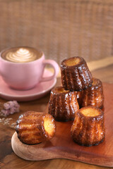 canele french dessert are stacked on a wooden cutting board with a cup of cappuccino with latte art behind