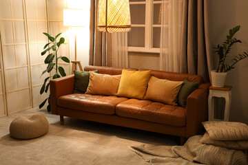 Interior of stylish living room with brown sofa, houseplants and glowing lamps at evening
