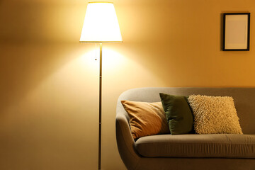 Interior of stylish living room with grey sofa and glowing standard lamp at evening