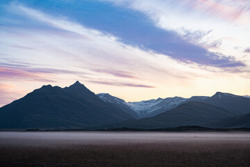 Twilight over Vatnajökull glacier in Iceland, with snow-covered peaks, pastel sky, rising crescent moon, and mist-covered plains evoking stillness and grandeur.