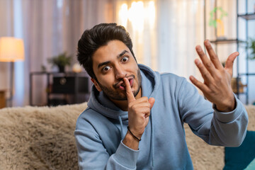 Shh be quiet please. Portrait of young Indian man presses index finger to lips makes silence...