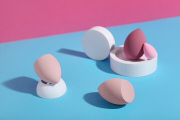 Decorative podiums with makeup sponges on colorful background