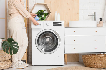 Young woman putting laundry detergent into modern washing machine in laundry room, closeup