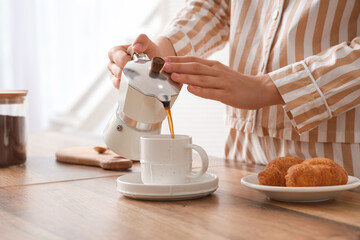 Young woman in pajamas pouring fresh espresso from geyser coffee maker into cup at home, closeup