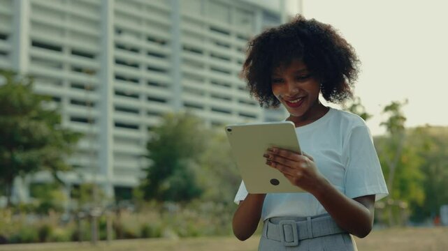 Portrait of pretty African American woman using tablet computer against office building on street. Female student scrolls internet in touchpad device on city square