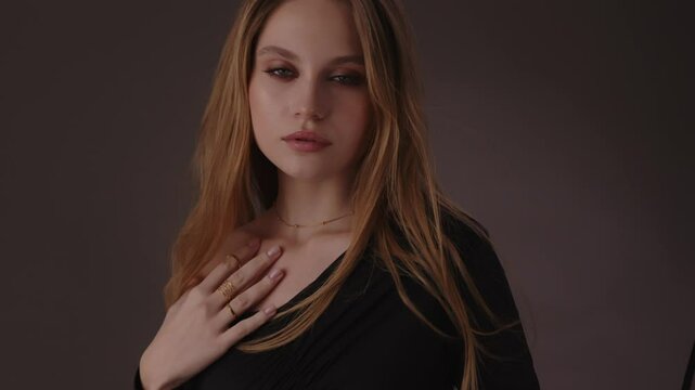 Beautiful girl with gold jewelry and loose hair in black clothes posing on a dark background. Beauty face and hair. Video 4k