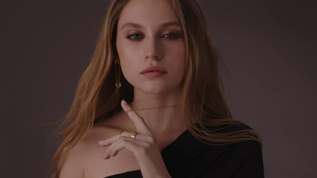 Beautiful girl with gold jewelry and loose hair in black clothes posing on a dark background. Beauty face and hair. Video 4k