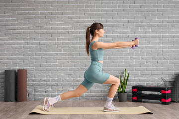 Sporty young woman with dumbbells doing aerobics in gym