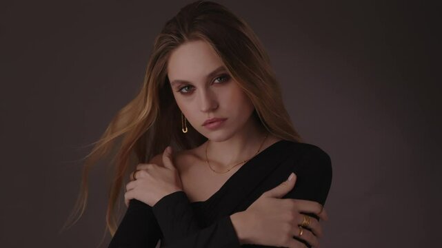 Beautiful girl with gold jewelry and loose hair in black clothes posing on a dark background. Beauty face and hair. Video 4k