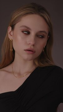 Beautiful girl with gold jewelry and loose hair in black clothes posing on a dark background. Beauty face and hair. Video 4k