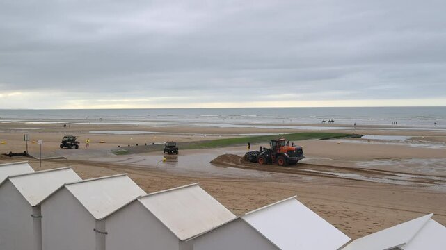 Beach, city of Cabourg, Normandy, a backhoe moves sand near the beach cabins, High quality 4k footage