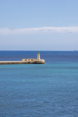 Lighthouse and St. Elmo Breakwater surrounded by calm blue water of Mediterranean Sea, Valletta, Malta