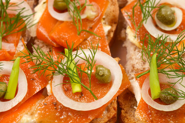An assortment of open-faced sandwiches featuring carrot slices prepared as vegan salmon, arranged in a clear container