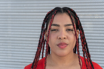 Young woman wearing red dress and braids posing in front of metal wall