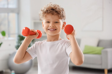 Sporty little boy exercising with dumbbells at home