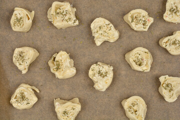 An overhead shot shows raw cheese and oregano puff pastry rolls arranged on parchment paper on a...