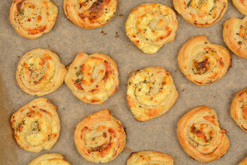 An overhead shot of golden brown cheese puff pastry rolls arranged on parchment paper on a baking sheet