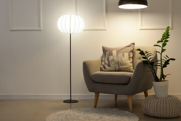 Interior of living room with armchair, pouf and glowing lamps in evening