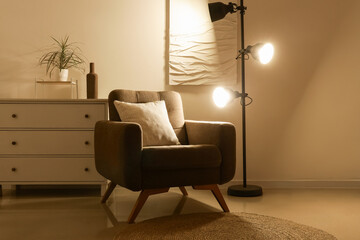 Interior of living room with armchair and glowing lamp in evening