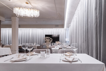 beautiful table decoration in restaurant. festive table setting in restaurant. white tablecloth on table, wine glasses, white plates, flowers in vase, candles are burning. romantic atmosphere