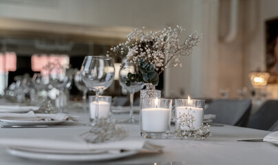 beautiful table decoration in restaurant. festive table setting in restaurant. white tablecloth on table, wine glasses, white plates, flowers in vase, candles are burning. romantic atmosphere