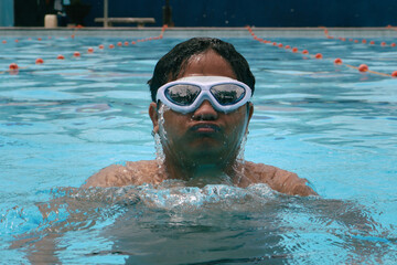 Naklejka premium Asian young man swimming at outdoor pool. Healthy lifestyle and wellness concept