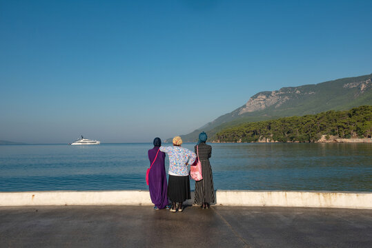 Muslim women visitors to the Turkish seaside town of Akyaka admire the beautiful view and expensive yacht moored in the bay. Turkish coast, Mugla. .