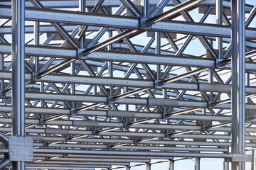 Fototapeta premium Metal construction texture pattern. Urban geometrical interlacing of bolted connections cross bars and beams of construction site over blue sky with clouds background.