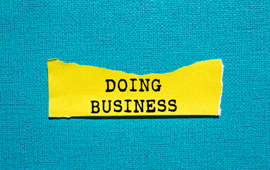 Doing business message written on ripped torn yellow paper piece on blue background. Conceptual...