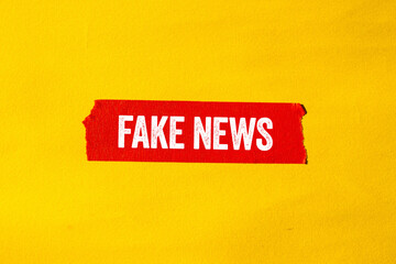 Fake news message written on ripped torn red paper tape on yellow background. Conceptual fake news...
