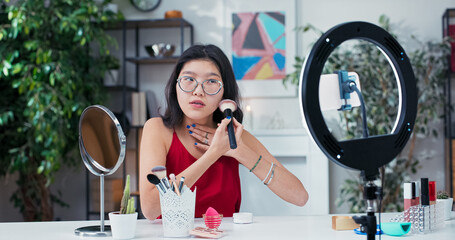 Stylish beauty creator applies rice powder on camera during a live video review, discussing...
