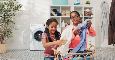 A cheerful daughter supports her mother in folding laundry, placing dry clothes aside while chatting in a bright bathroom, bonding through shared household responsibilities.