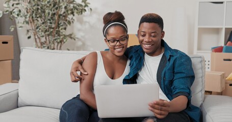 A cheerful couple sits on the sofa with a laptop, exploring interior design ideas. They giggle and...