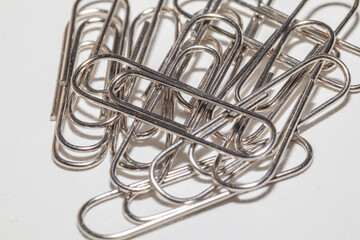 A pile of shiny silver paper clips on a white background.