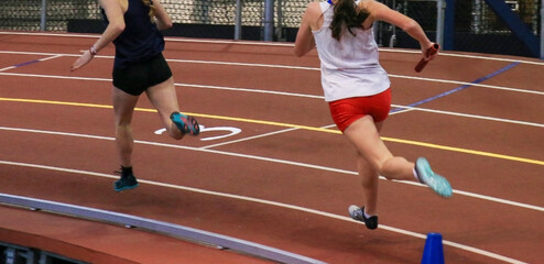 Two girls holding batons racing fast on an indoor track